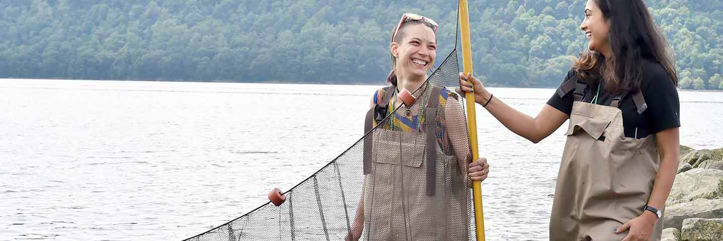 two students laughing holding a seining net in hipwaders